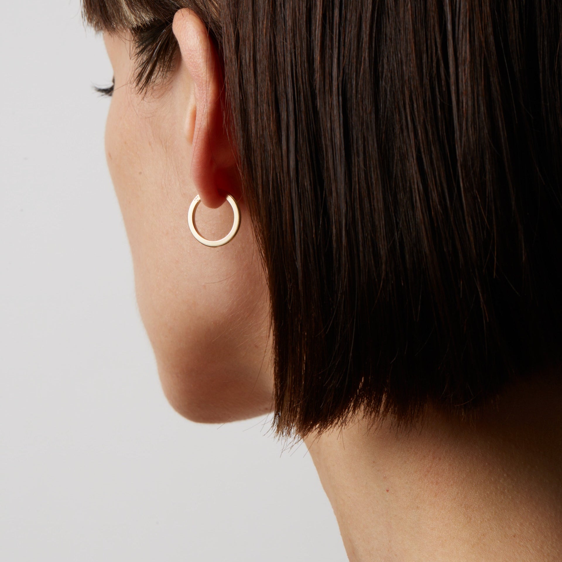 Close-up of a person wearing a gold hoop earring against a light background