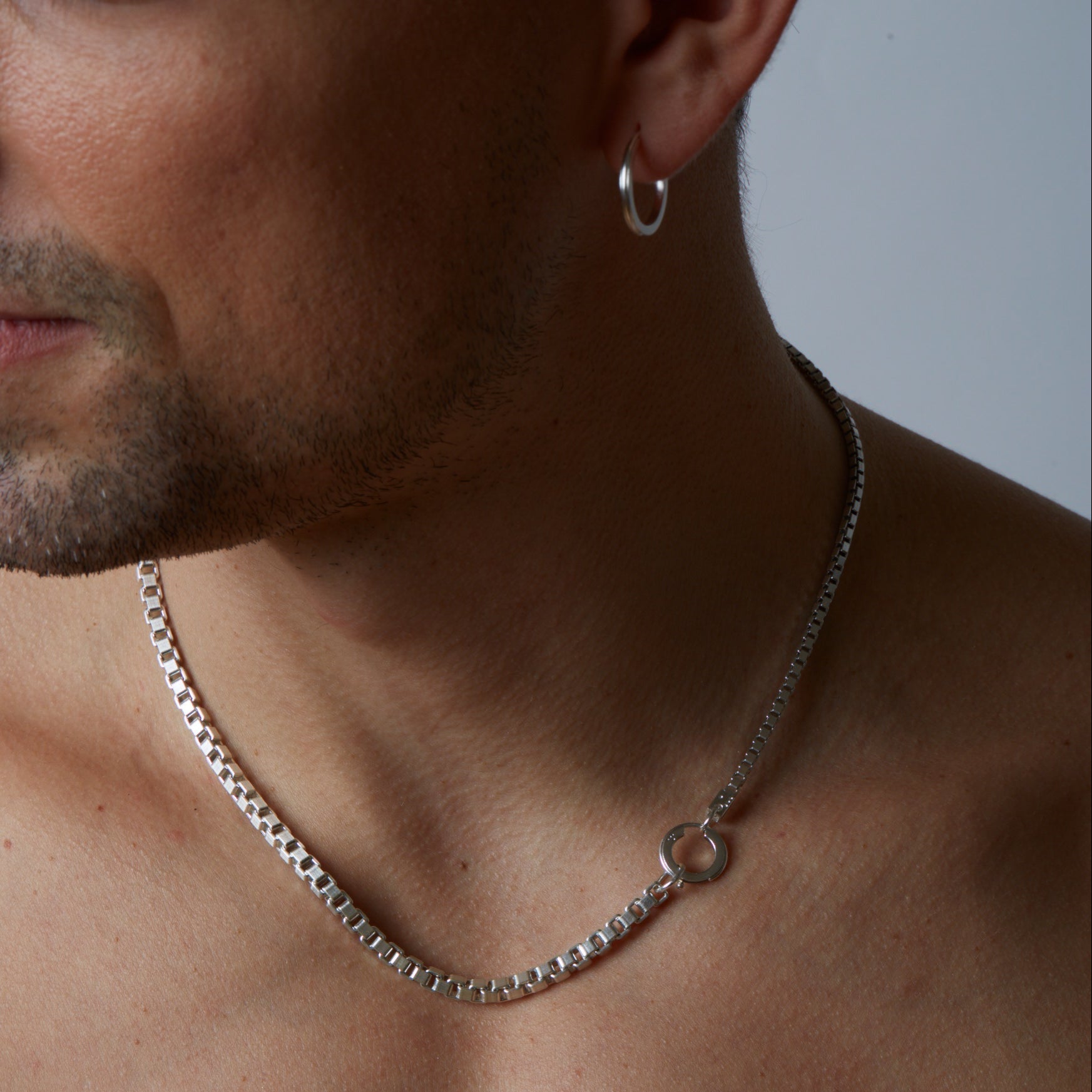 Close-up of a person wearing a silver chain necklace with a neutral background