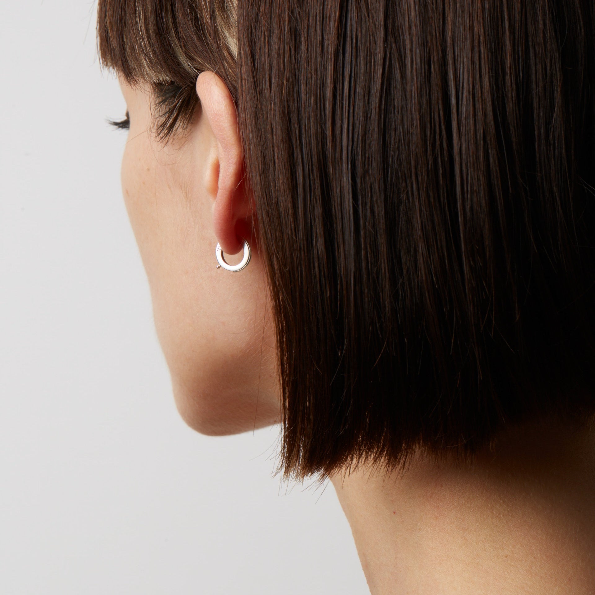Close-up of a person wearing a silver hoop earring against a neutral background
